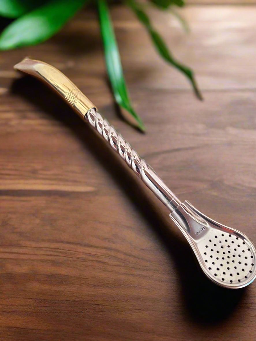 Metallic bombilla on a wooden surface with green leaves in the background