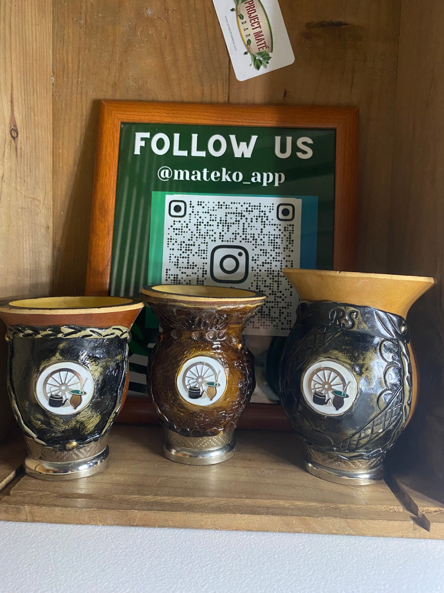 Three porongo gourds with decorative metal designs on a wooden surface with a blurred green background