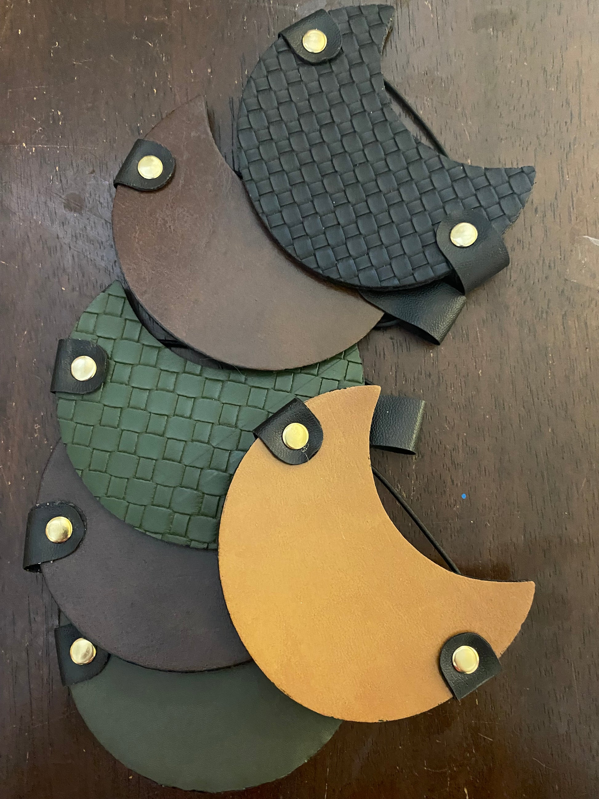 A collection of yerba mate covers in beige, black, brown, and green colors, featuring elastic bands and metal eyelets for attachment.