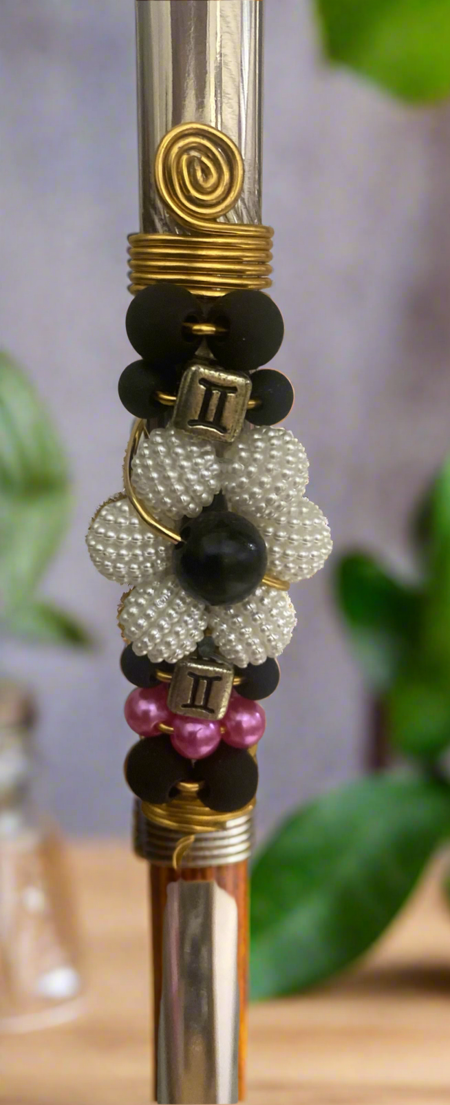 A close-up image of a stainless steel bombilla  with a floral pattern, featuring various colored beads and a yellow gold-tone band.