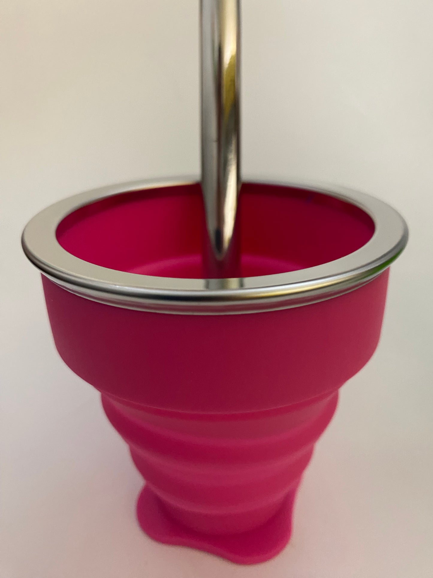 A fusia silicone collapsible cup with a metallic top, likely used for serving or drinking Mate.