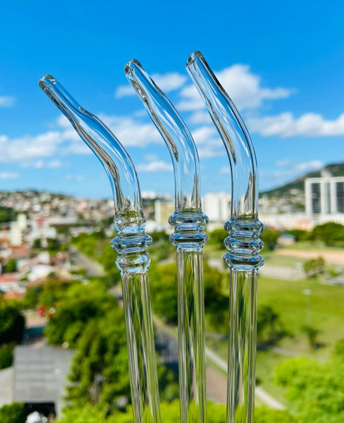 Three clear glass straws with filters, designed for drinking mate, set against an urban landscape background.