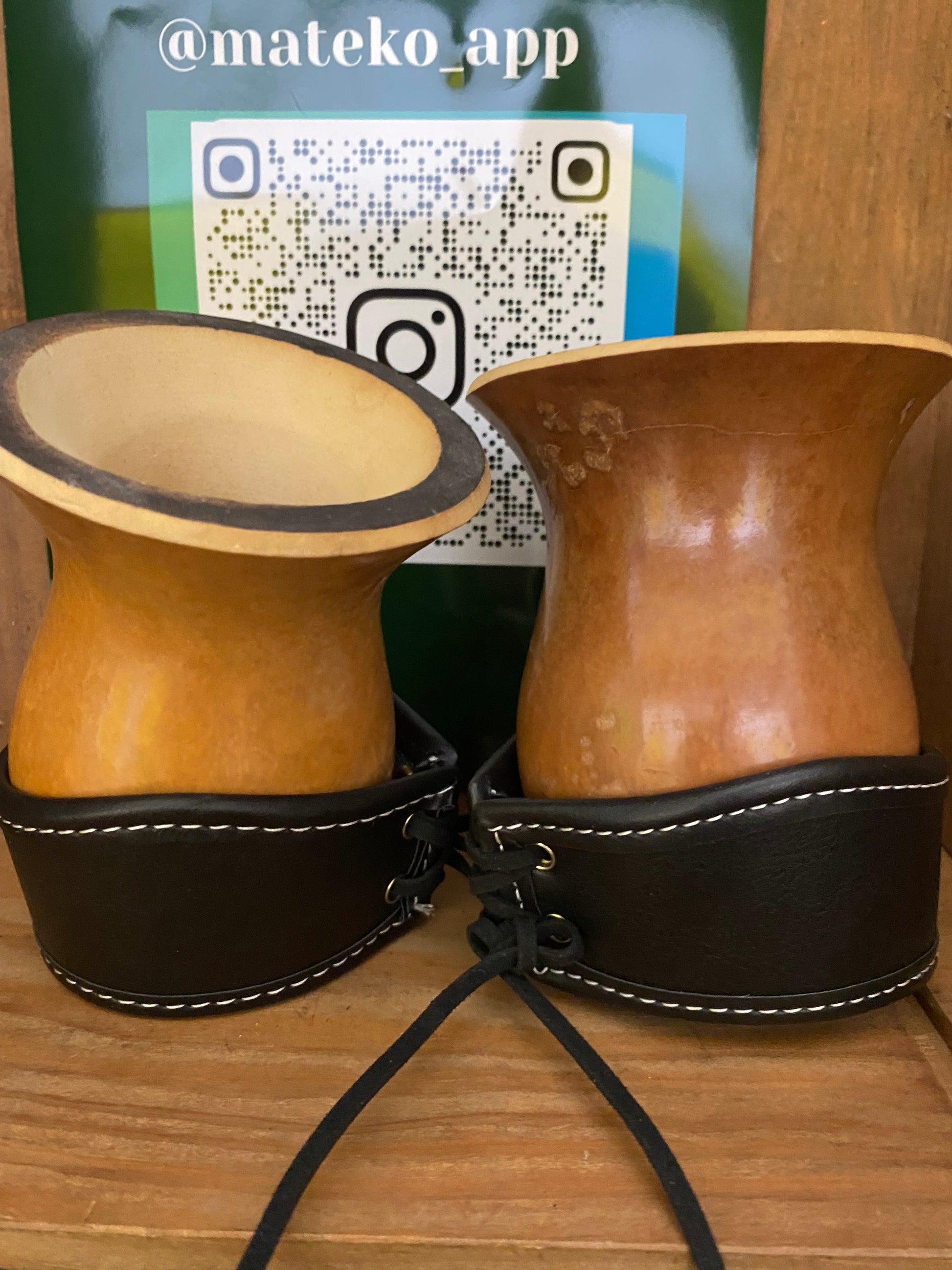 Porongo gourd with leather strap on a wooden surface, with a phone displaying a QR code in the background.