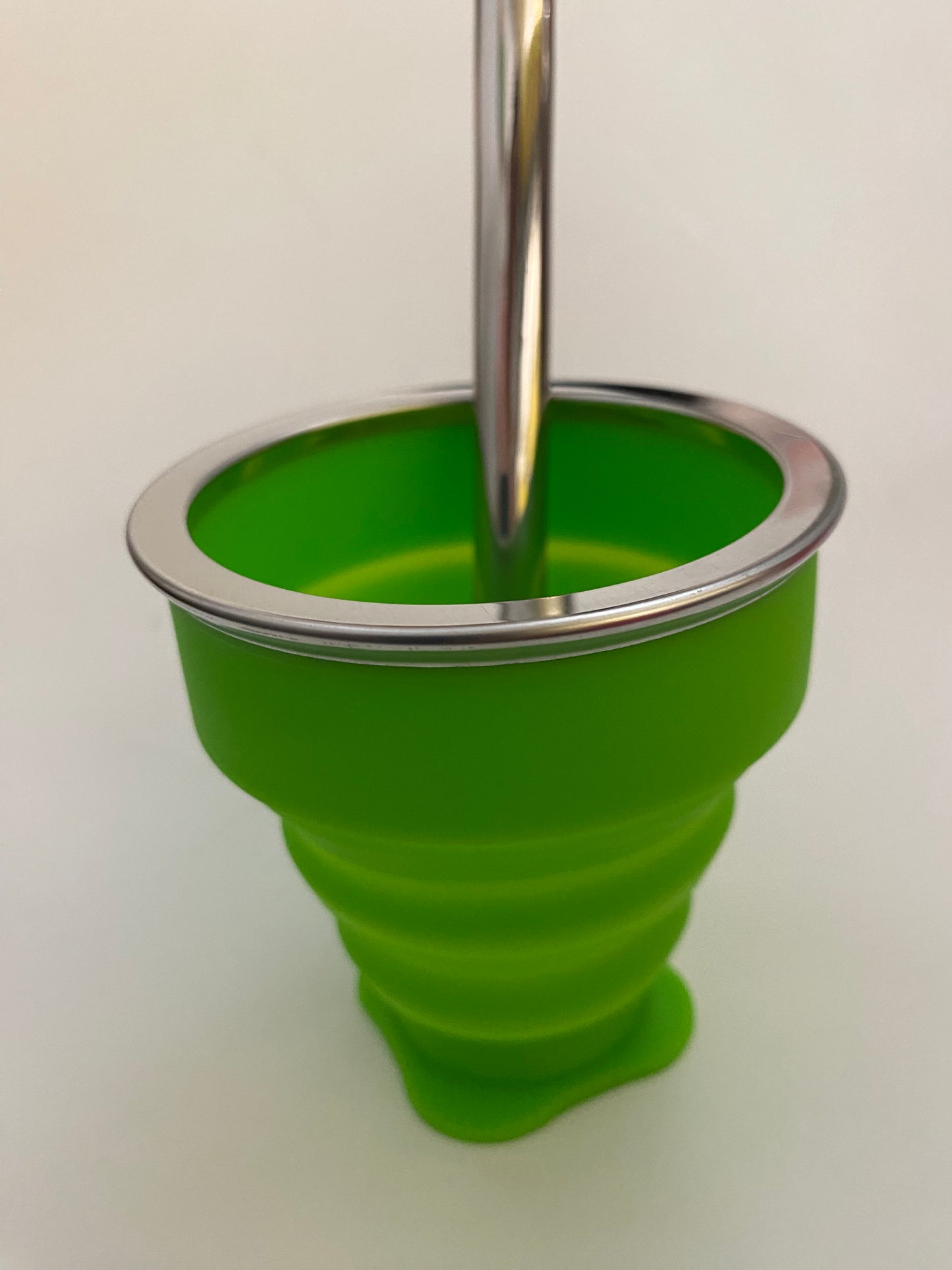 A green silicone collapsible cup with a metallic top, likely used for serving or drinking Mate.