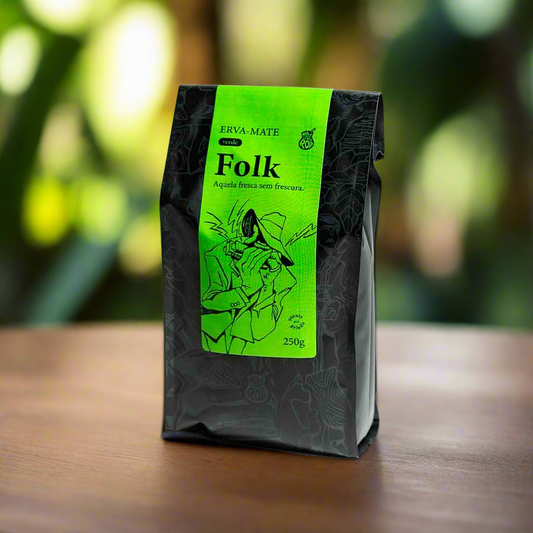 A package of Matte N Roll Folk yerba mate with a green label, displaying the brand and product name, placed on a wooden surface with a green, leafy background.