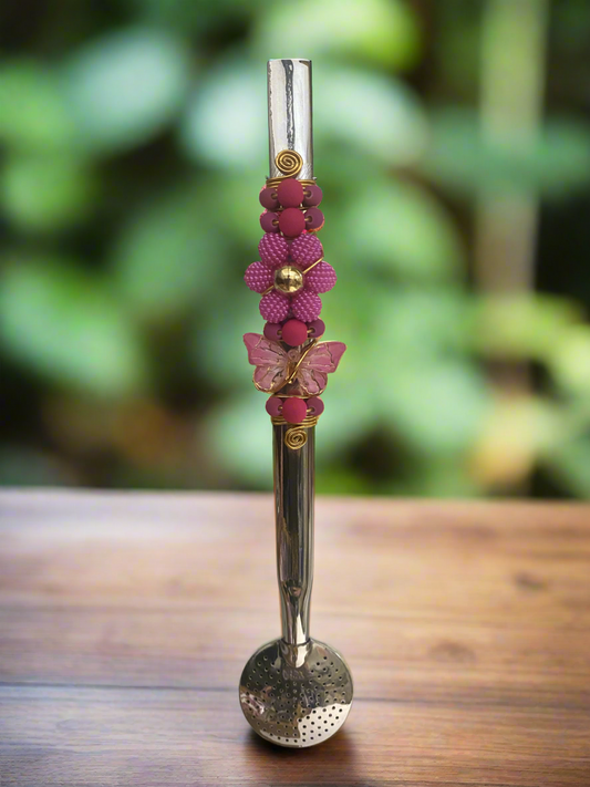 A stainless steel bombilla with a multicolored beaded handle and a decorative butterfly and flower on the top.