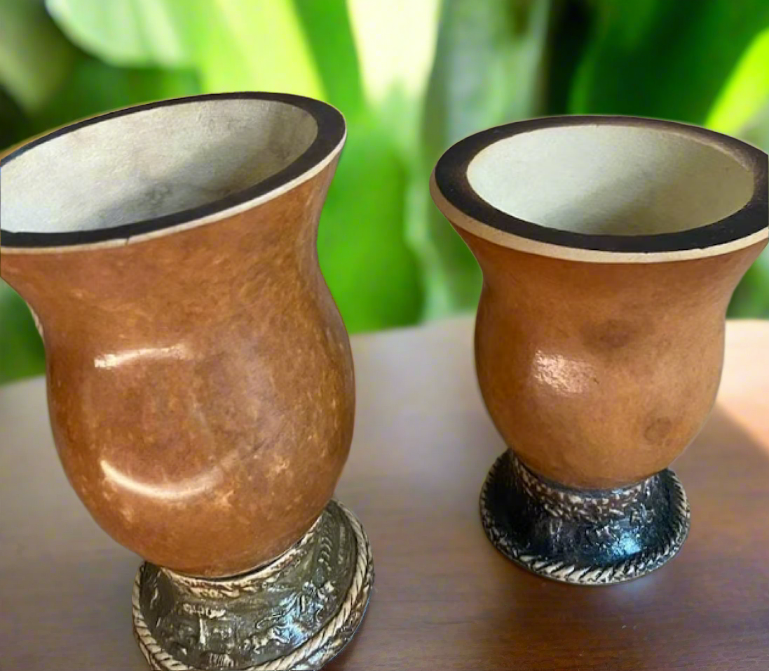 Two yerba mate gourd cuias against a blurred green background.
