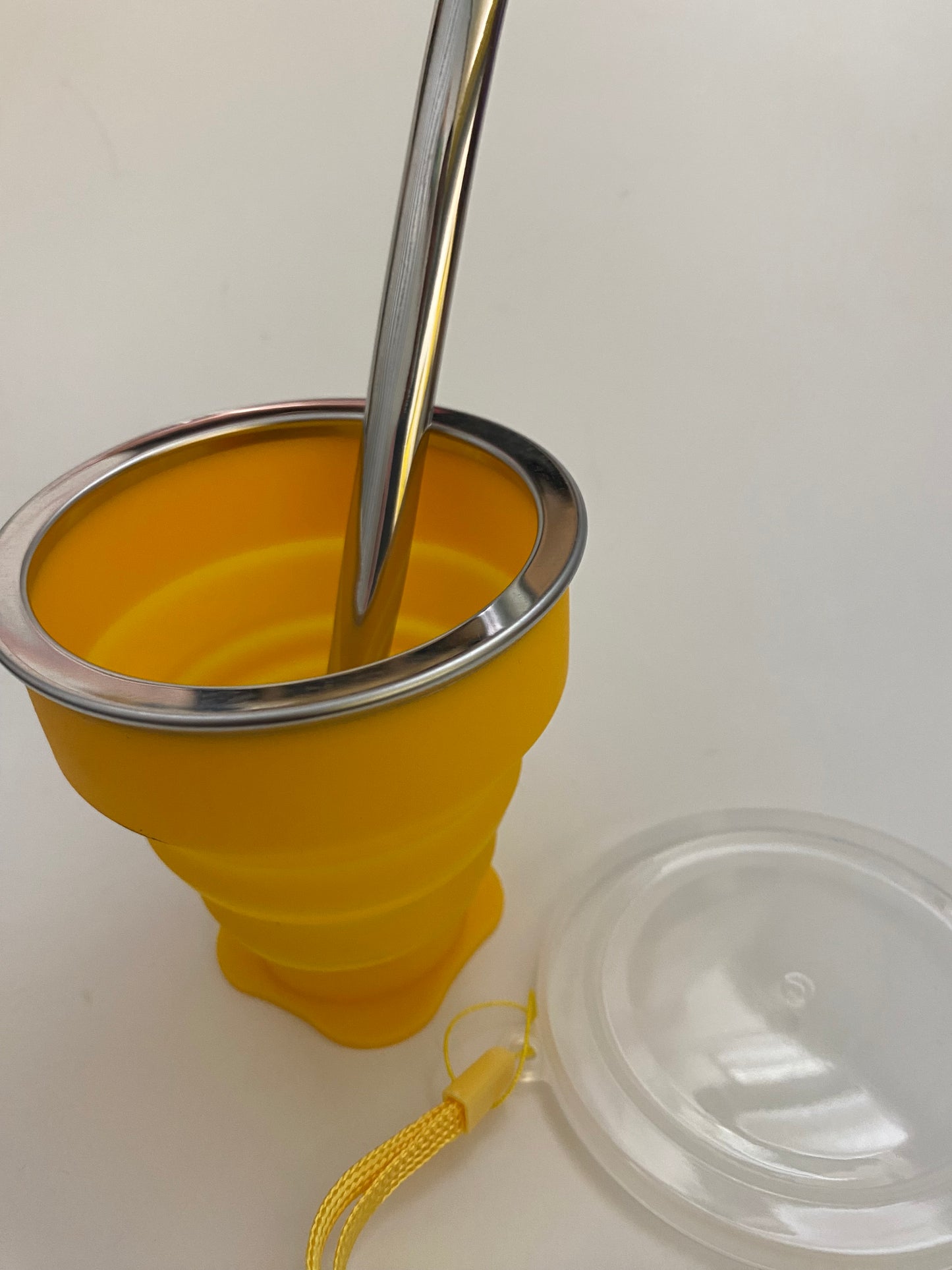 A yellow silicone mate with a metal straw inserted and a plastic top. 