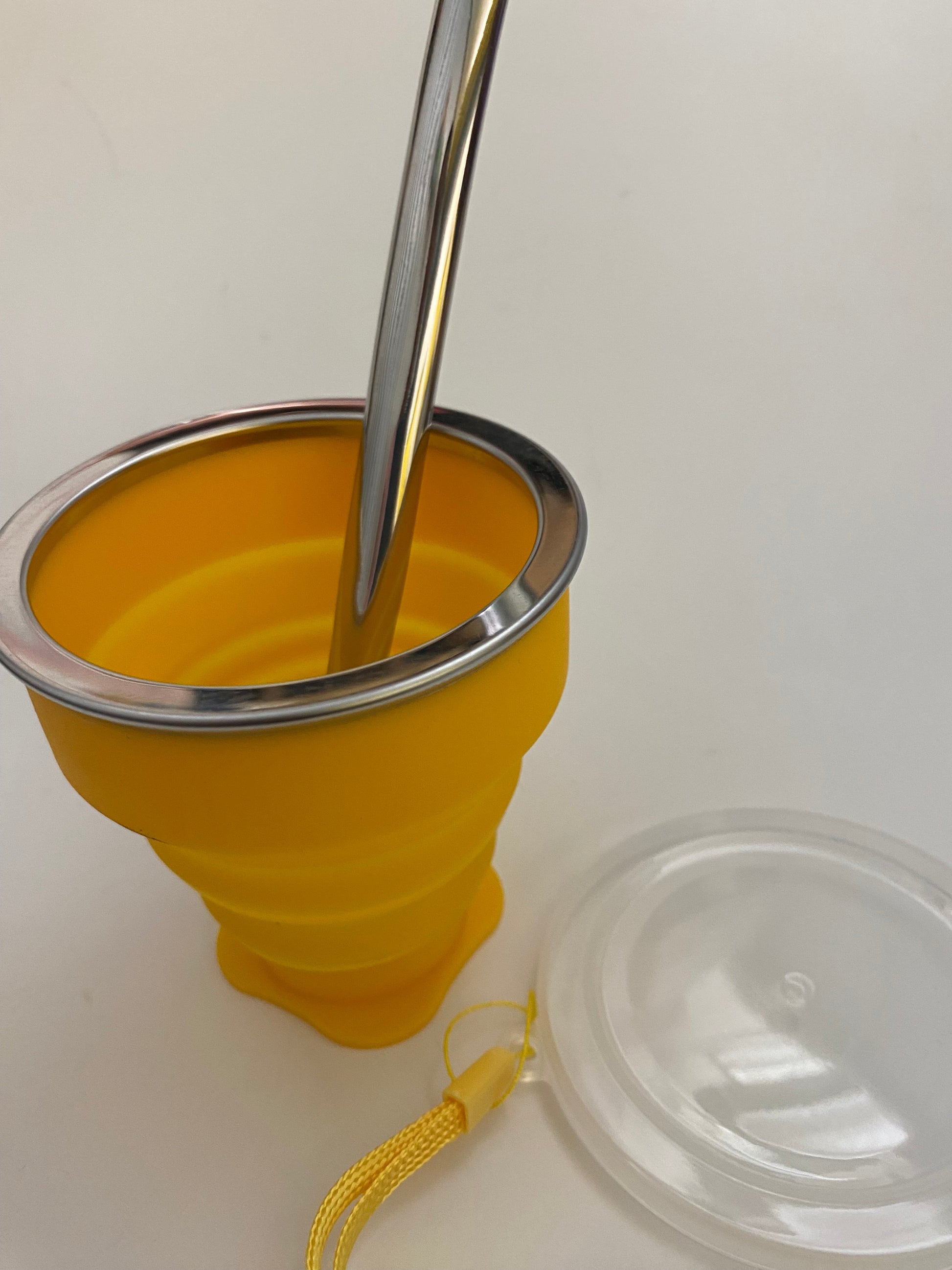 A yellow silicone mate with a metal straw inserted and a plastic top. 