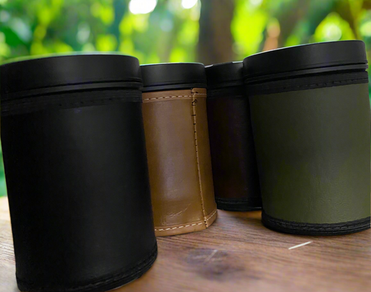 Four cylindrical containers with black lids on a wooden surface with a blurred green background