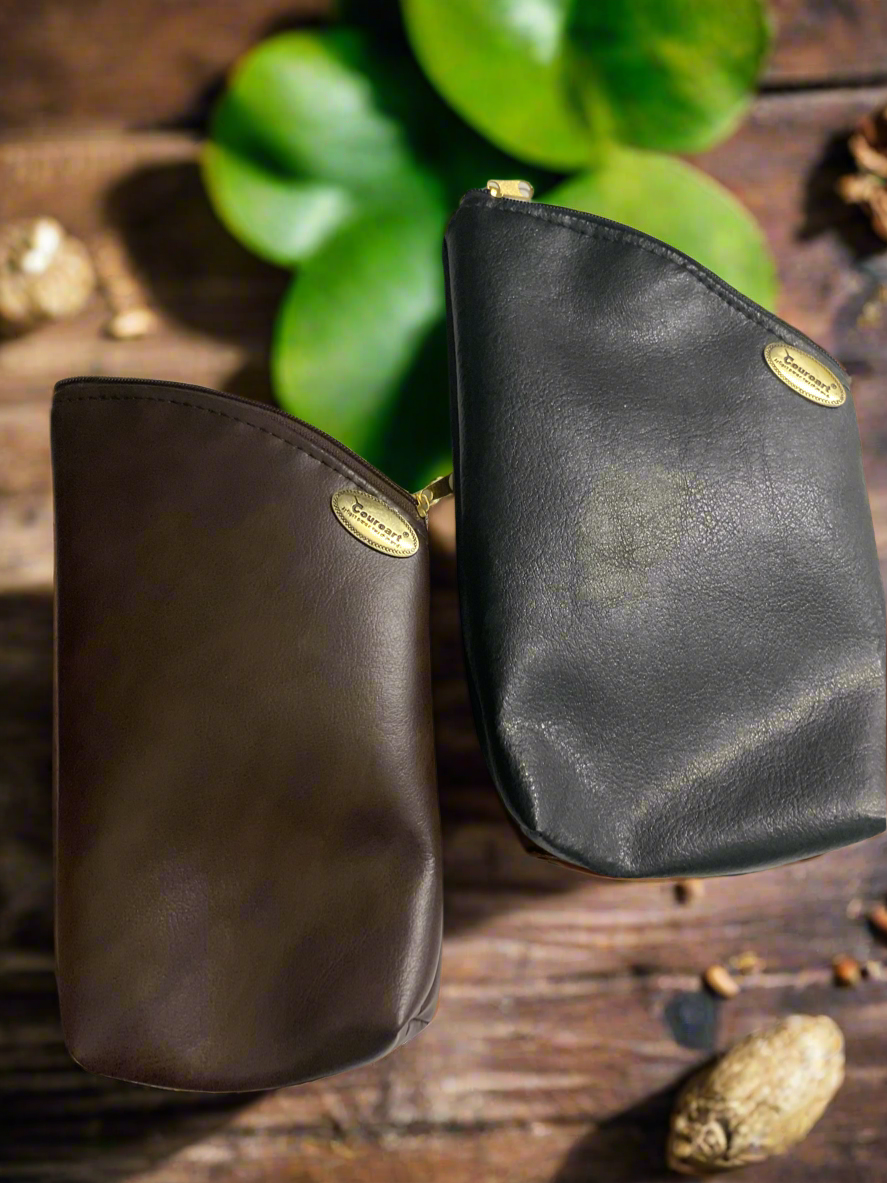 Two leather yerba pouches, one brown and one black, displayed on a wooden surface with a green plant in the background.