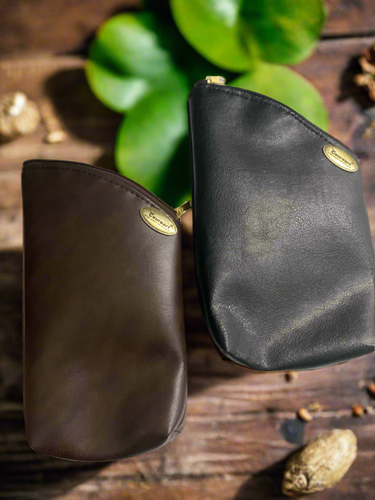 Two leather yerba pouches, one brown and one black, displayed on a wooden surface with a green plant in the background.