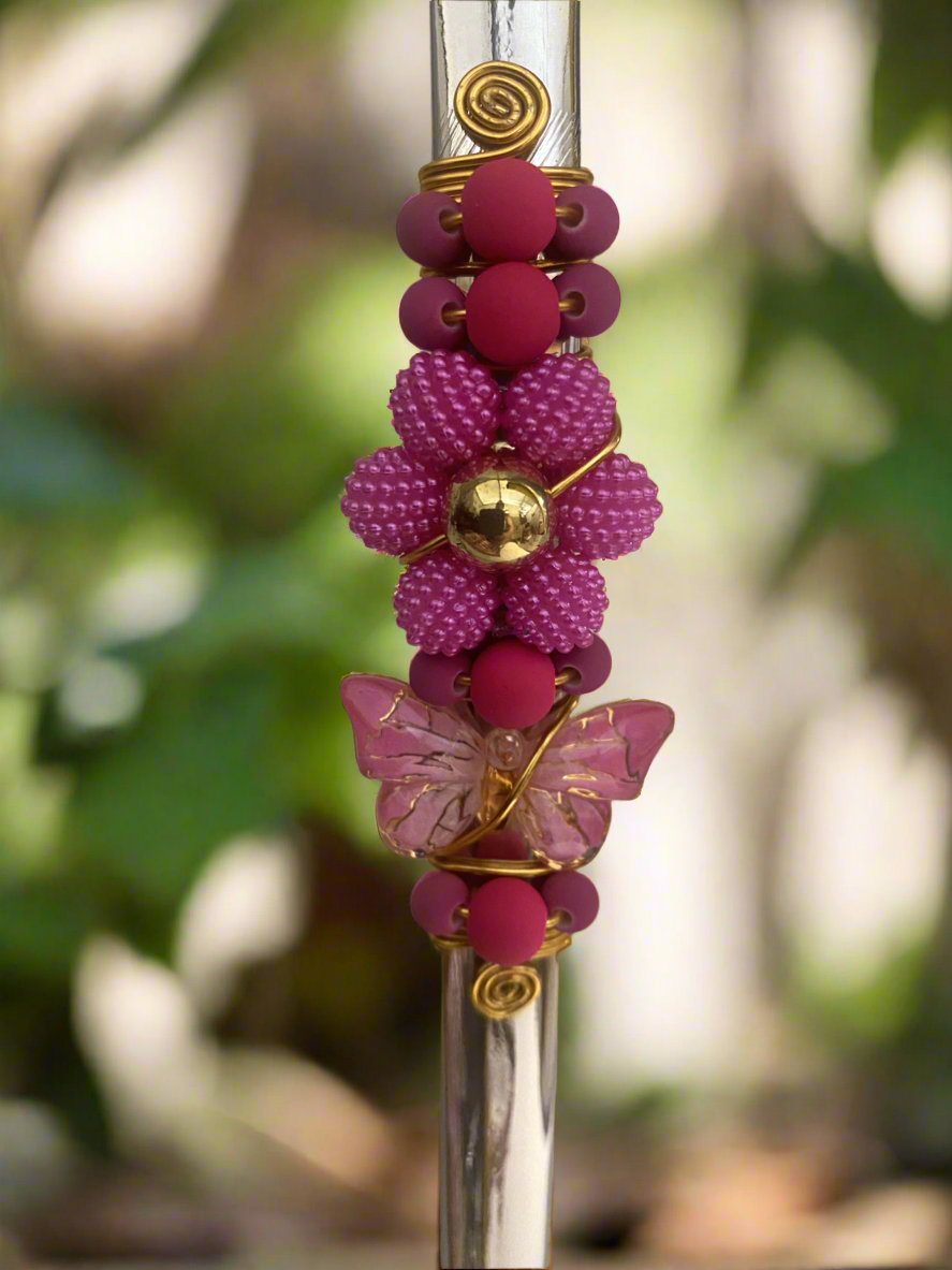 A zoom in on a bombilla with a multicolored beaded handle and a decorative butterfly and flower on the top.